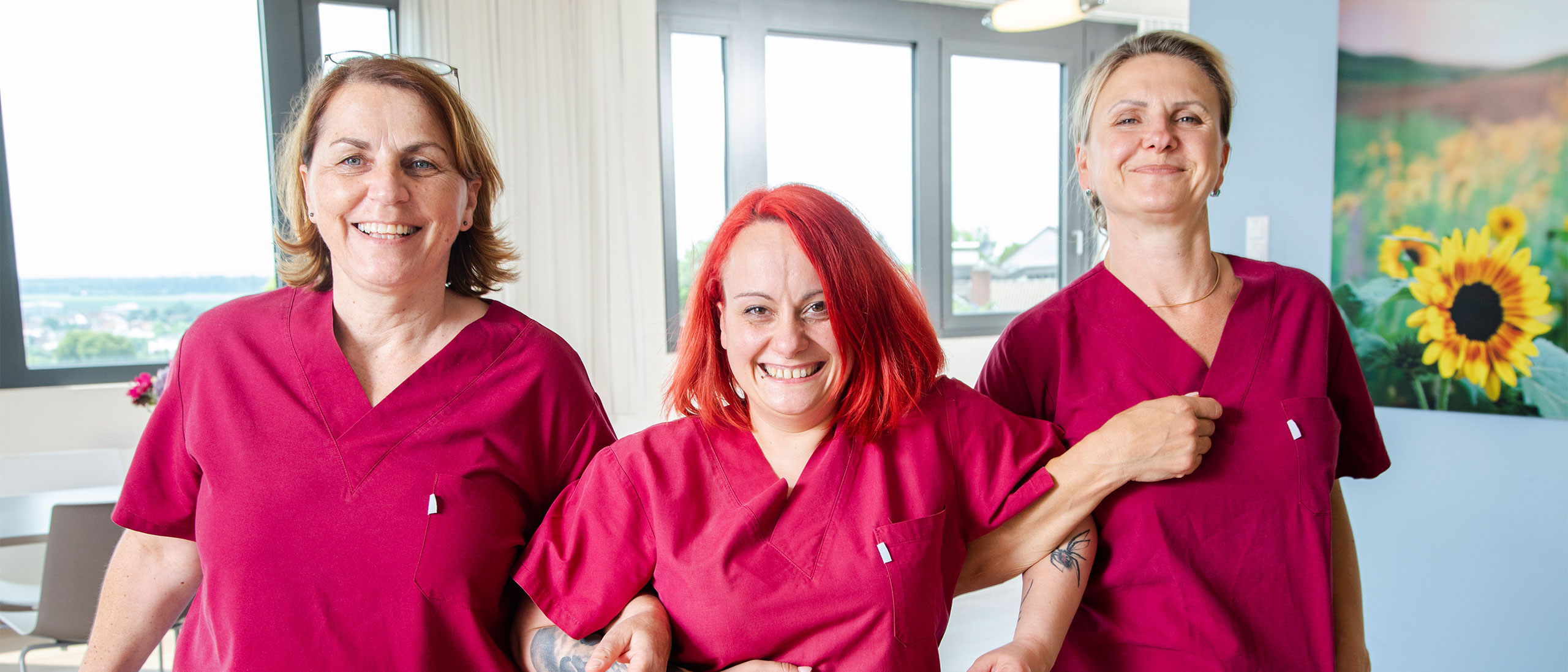 Drei Pflegekräfte in roter Arbeitskleidung